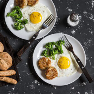 Fried eggs, broccoli, chicken meatballs, homemade whole wheat bread - tasty simple dinner. On a dark background, top view